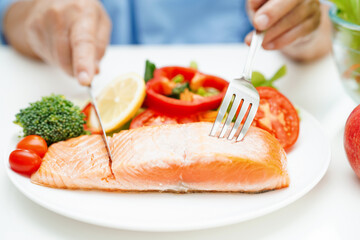 Wall Mural - Asian elderly woman patient eating salmon stake and vegetable salad for healthy food in hospital.