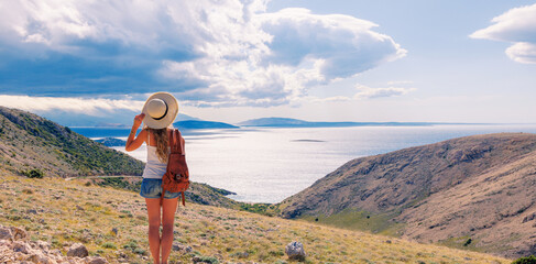 Wall Mural - Woman with bag and hat enjoying panoramic view of the sea at sunrise- travel, vacation,wanderlust concept