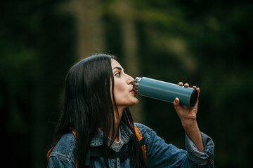 Wall Mural - Solo Latin adventurer resting on a tree stump, surrounded by the beauty of a dense forest, quenching her thirst with a water bottle during a mountain hike