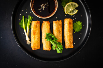 Wall Mural - Vegetable filled spring rolls and soy sauce on black wooden table
