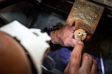 Jeweler hands setting a diamond into a ring with a burin in a jewelry workshop. Goldsmith working and creating a gold jewel.