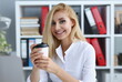 © H_Ko - Smiling business woman drinking coffee from a paper cup in the office portrait looking into the camera. Holding in her hand and resting during a break.