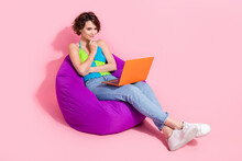 Full Length Photo Of Thoughtful Cute Young Woman Watch Youtube Series Using Netbook Sitting Pouf Outdoors Isolated On Pink Color Background