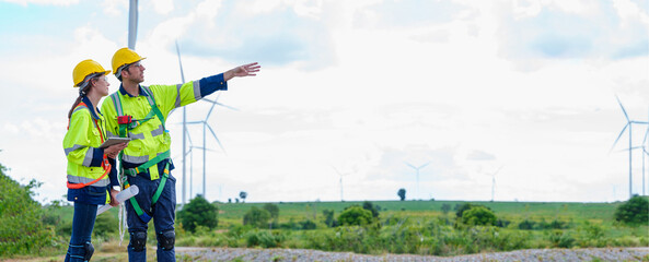 Young Maintenance engineer team worker building looking for wind turbines blueprint drawings and point finger on windmill field farm Alternative renewable energy for clean energy concept.