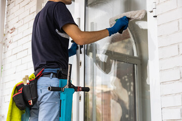 Wall Mural - Male professional cleaning service worker in overalls cleans the windows and shop windows of a store with special equipment