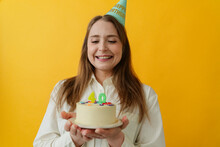 Happy woman wearing party hat holding birthday cake