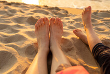 Mother And Daughter With Barefeet Relaxing On Sand At Beach