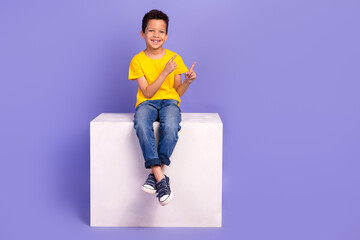 Wall Mural - Full body photo of charming young boy sit white podium point empty space wear yellow outfit isolated on purple color background