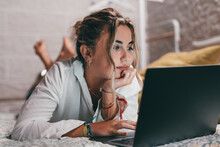 Close up of one young pretty woman using laptop indoor at home lying on the bed surfing the net. Millennial teenager having fun online studying. .