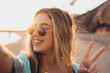 © Daniel - Portrait close up of one young beautiful attractive blonde young girl holding camera and taking selfie picture at the beach enjoying outdoors free time with sunset in the background..