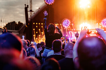 Wall Mural - Stage lights against a happy woman with raised arms while enjoying a concert at a music festival