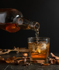 Wall Mural - Whiskey with ice on a black table with dried-up oak leaves.