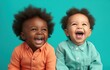 Two joyful children laughing against a teal background.