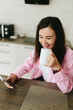 © Mila - A young girl with black hair in a pink shirt sits at a table with a phone and a white mug in a cozy room with brown brick. Woman working, talking on the phone, drinking coffee in a modern cafe.Morning