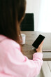 © Mila - A young girl with black long hair in a pink shirt and white top sits at a table with a phone and a white mug in a cozy room. A white mug and a phone in the hands of a girl. Morning business woman