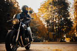 motorcyclist in a helmet with a classic motorcycle in the fall. Stylish motorcyclist in a leather jacket and gloves.