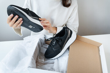 A young girl sits at a table and looks at her new sneakers from a box. Online shopping, payment by card, delivery by courier.