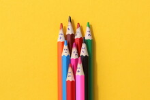 Multi-colored Pencils With Painted Faces Lie On A Yellow Background.	