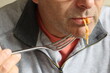 Close-up of the lower part of a man's face, sucking on a single cooked spaghetti strand while holding a fork near his mouth.