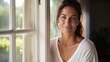 © Restyler - Beautiful 45 year old happy woman in loose home clothes at the window. Portrait of a smiling lady. Feminine beauty.