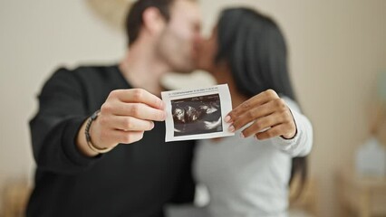 Wall Mural - Beautiful couple sitting on bed holding baby ultrasound kissing at bedroom