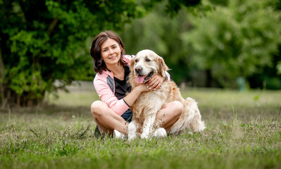 Sticker - Pretty girl hugging golden retriever dog sitting in grass at nature. Beautiful young woman with purebred pet doggy labrador in park at summer