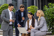 © Liubomir - Four business people in business clothes outside office building happily chatting on lunch break, diverse team of men and women together, smiling and friendly communication.