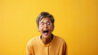 Young older mature middle aged woman wearing glasses and yellow shirt over yellow background excited and surprised with wow expression, excited face.