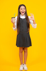 Canvas Print - Amazed teen girl. Teenager girl holding a hot cup of coffee or tea. Child with takeaway cup on yellow background, morning energy drink beverage. Excited expression, cheerful and glad.