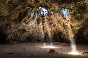 quadiriki cave in arikok national park, aruba. sunbeams extend from openings in the cavern roof to t