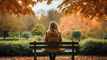 Back View Of A Young Woman Sitting On A Bench In The Park At Autumn