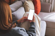© Farknot Architect - Mockup image of a woman holding mobile phone with blank desktop white screen while lying on a sofa at home