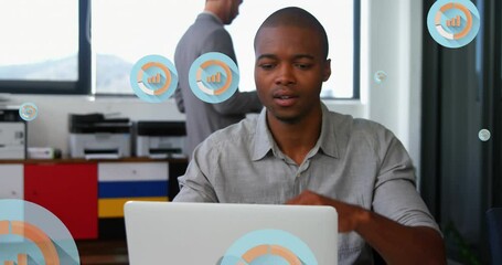 Wall Mural - Animation of multiple graph icons over tired african american man looking at laptop in office