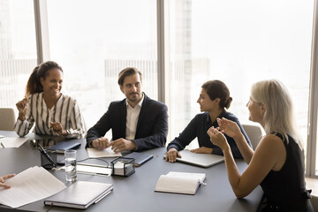 Wall Mural - Senior business team leader speaking to diverse employees at meeting table, listening to creative ideas, offers, brainstorming with diverse young group, discussing work plan, teamwork strategy