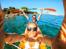 Overjoyed Couple Of Caucasian Adult Tourist Man And Woman Taking Selfie Picture Inside A Kayak Canoe With Blue Clean Sea Ocean Water And Coastline In Background. Travel And Summer Holiday Vacation
