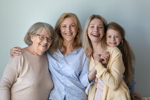 Happy Kid, Young Mother, Mature Grandmother, Senior Great Grandma Portrait. Girl And Women Of Four Female Generations Standing At Grey Background, Hugging With Love, Smiling, Laughing
