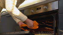 A woman taking a hot baking pan from the oven, using safe silicone mitts during her cooking hobby