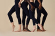 Young fit sporty diverse women wearing sportswear cloth black leggings fitness outfit pants standing in row on beige, legs feet close up shot. Multicultural girls four models isolated on background.