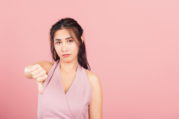 Wall Mural - Portrait Asian beautiful young woman unhappy, negative gesture showing finger thumbs down or dislike sign, studio shot isolated on pink background, Thai female rejection unlike with copy space