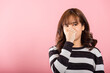 Portrait of an Asian woman, unhappy with a disgusted expression, pinches her nose due to a foul smell. Studio shot isolated on pink, illustrating a healthcare concept.