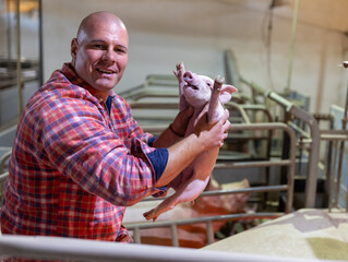 Farmer holding cute piglet in pigpen