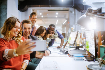 Wall Mural - Diverse group of coworkers taking a selfie on a smartphone in the office of a startup company