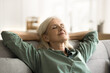 © fizkes - Positive tranquil elderly woman relaxing on couch with closed eyes, smiling, stretching body, leaning on soft back with open elbows, enjoying leisure, calm lazy break at home, breathing fresh air