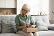 © fizkes - Cheerful old retired consumer woman getting purchase from Internet store, holding paper box on lap, using smartphone, giving positive review, feedback to delivery logistic service, Internet store