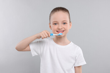 Wall Mural - Happy girl brushing her teeth with toothbrush on light grey background