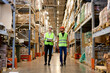 © alfa27 - Retail Warehouse full of Shelves with Goods, Two Young Caucasian Male Workers Supervisors in Working Uniform and Helmet Discuss Product Delivery. Men Walking and Having Talk In Warehouse