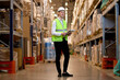 © alfa27 - logistic business, shipment and people concept. male in helmet with clipboard checking goods at warehouse, counting and controlling distribution. confident hardworking caucasian worker in uniform