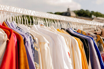 Choice of fashion clothes of different colors on hangers in a retail shop. Flea market with old clothes outside. Reduce Reuse Recycle concept