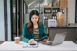 © laddawan - Confident business expert attractive smiling young woman typing laptop ang holding digital tablet on desk in office.