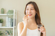 © KMPZZZ - Dietary supplement, asian young woman, girl hand holding medical pill capsule, take or eat vitamin C, D for treatment for skin, hair and nail strengthen with glass of pure water at home, healthcare.